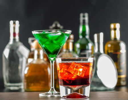 Colorful drink on the background of bottles in original shapes, cocktail drink with ice cubes, party nightの写真素材