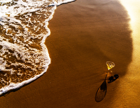 drink in a martini glass washed by sea water on a sandy beach, relax on the beach, refreshing drink during your vacation, summer timeの写真素材