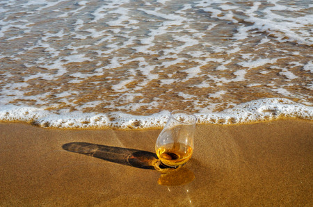 a glass of whiskey single malt on the sand washed by the waves, a glass of tasting, relax on the beach, vacationの写真素材