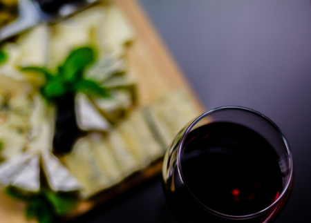 Red wine and set of different cheeses on a wooden board, delicious snack, healthy and exclusive foodの写真素材