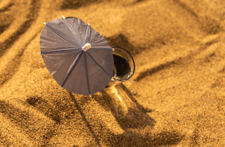 A glass of water on a sandy beach with umbrellas for drinks, summer relaxの写真素材