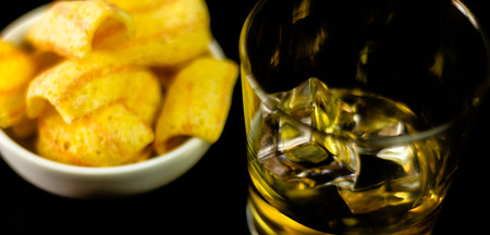 Glass of whiskey with ice cubes and salty snacks on the background of the bar, party timeの写真素材