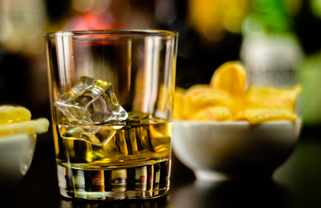 Glass of whiskey with ice cubes and salty snacks on the background of the bar, party timeの写真素材