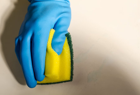 Hand in rubber gloves cleaning the surfaces of ceramic tiles, safe and hygienic cleaning, keeping...