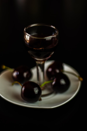 Cherry liqueur and juicy ripe cherries on the table in  the bar, an elegant serving of sweet drink in the restaurant, a traditional drinkの写真素材