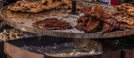 Different types of meats and sausages stacked on a big grill while cooking, great grilling