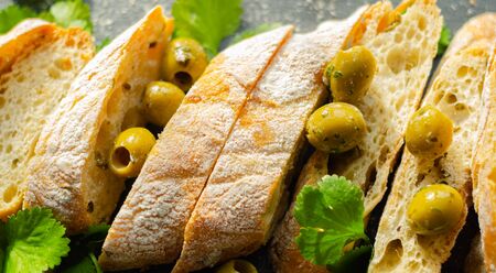 Baguette stuffed with olives, cut with fresh green olives and parsley, served on a stone plate, healthy appetizerの写真素材