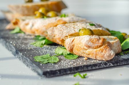Baguette stuffed with olives, cut with fresh green olives and parsley, served on a stone plate, healthy appetizerの写真素材