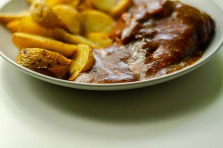 Cooked chicken breast fillet in a barbecue sauce, topped with smoked bacon and Red Leicester cheese and served with potato wedges, traditional english mealの写真素材