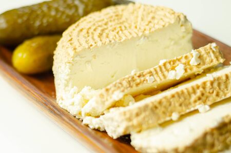 Smoked cottage cheese, brined cheese cut with pickled cucumber on a wooden plate, a traditional and natural food productの写真素材