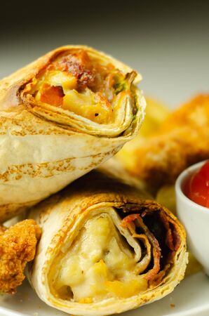 Tortilla wrap with chicken and beechwood smoked bacon served with chicken nuggets and chips on the white plate, tasty foodの写真素材