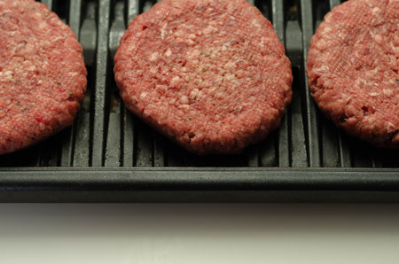 Seasoned beef burgers with a pinch of salt and black pepper on the grill, cookout