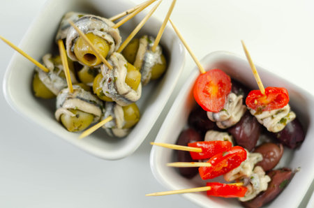 The traditional Spanish appetizers of olives, tomatoes and anchovies in a white ceramic bowls,...