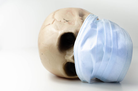 Scary human skull wearing a medical mask, symbolic depiction of death from viral epidemic, coronavirusの写真素材