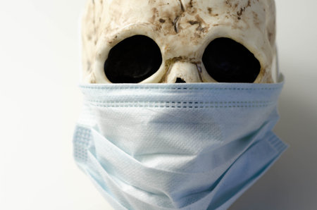 Scary human skull wearing a medical mask, symbolic depiction of death from viral epidemic, coronavirusの写真素材