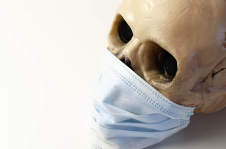 Scary human skull wearing a medical mask, symbolic depiction of death from viral epidemic, coronavirusの写真素材