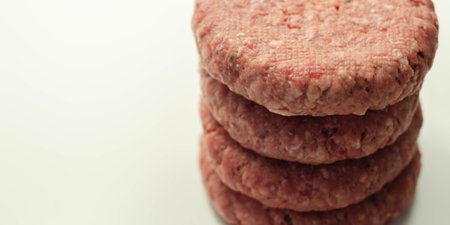Raw beef burgers with a pinch of salt and black pepper on the white background,  prepared meat for...