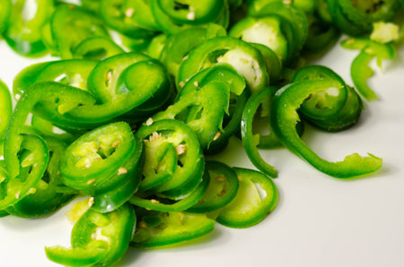 Fresh sliced green jalapeno peppers on a white background, spicy flavor ingredient in many dishes,...