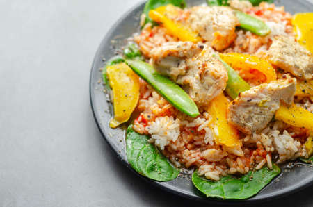 Cooked chicken breast pieces with peppers, sugar snap peas, and baby leaf spinach in a spicy sweet and sour sauce with fragrant rice, diet mealの写真素材