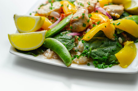 Cooked chicken breast pieces with peppers, sugar snap peas, and baby leaf spinach in a spicy sweet and sour sauce with fragrant rice, diet mealの写真素材