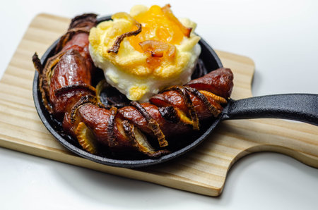 Grilled sausage with onion and egg in a cloud, all served on a cast iron pan, attractively served mealの写真素材