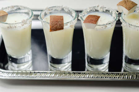 Coconut cocktail in drink shot glass based on the rum decorated with coconut flakes served on a silver tray, white drink shotsの写真素材
