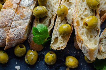 Baguette stuffed with olives, cut with fresh green olives and parsley, served on a stone plate, healthy appetizerの写真素材