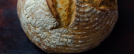 Traditional round loaf of bread baked according to a classic recipe, served on a wooden board,...