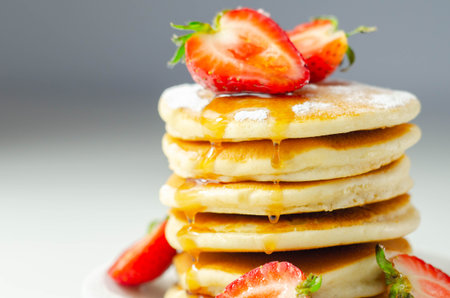 Delicious pancakes stacked with fresh sweet strawberries, topped with maple syrup, sweet breakfast