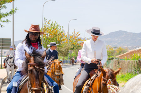 NERJA, SPAIN - 15 MAY 2022 Women in flamenco dresses and men on Andalusian horses dressed in their...