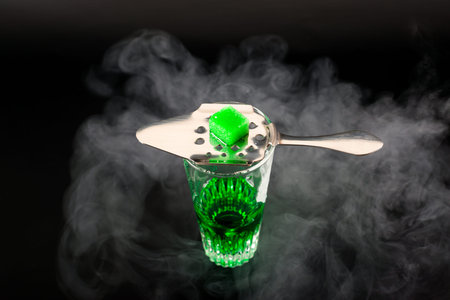 Green flavoured vodka called Absinthe served in a shot glass with a special spoon with white sugar...