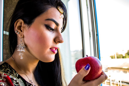 A girl in an Indian dress is holding a red apple in her handsの写真素材
