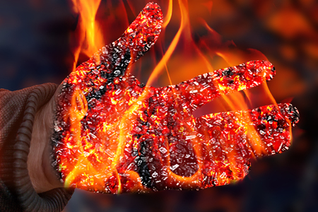 A burning man's hand covered with coal on a blurred fire backgroundの写真素材