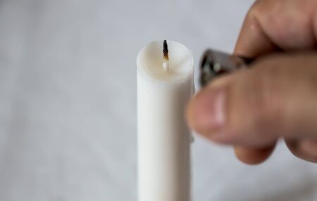 Hand with a burning lighter lights a white candle on a white backgroundの写真素材