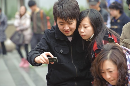 CHENGDU - FEB 7: A young couple looking at the pictures just taken on a busy pedestrian shopping street in downtown during chinese new year on Feb 7, 2011 in Chengdu, China.のeditorial素材