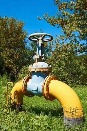 Large bent metal gas pipe with a valve on a green lawnの写真素材