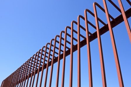 Fragment of fence with bent metal rods against a blue skyの写真素材
