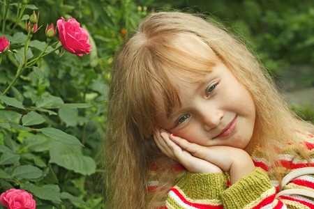 Beautiful small Caucasian girl in park near the rose bushの写真素材