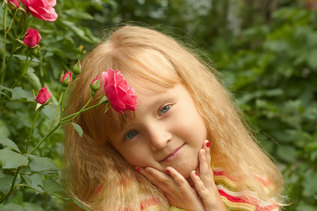 Beautiful little Caucasian girl in park near the rose bushの写真素材
