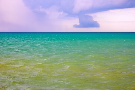 Thick cumulonimbus clouds over the sea with a turquoise and yellowish surface illuminated by the sunの写真素材