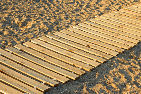Long wooden mat made from new parallel planks lying on a sandy beachの写真素材