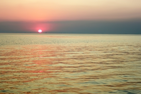 Red sun in the clouds near the horizon over the sea bayの写真素材