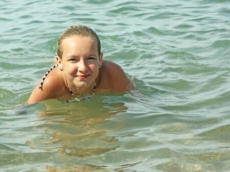 Smiling teenage girl swimming in sea water in warm sunny weatherの写真素材
