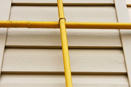 Two mutually perpendicular yellow gas pipes on a background of a wall covered with beige siding