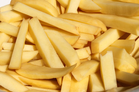 Heap of chopped pieces of raw potato strips for cooking potato chips, close-up, bright sinlight