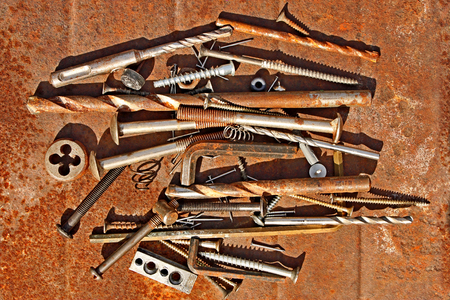 Many different steel and other metal objects on the rusty iron sheet close-up, in bright sunlightの写真素材