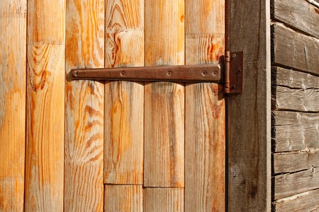 Wooden door of the old barn hanging on long iron hinge close-up, in bright sunlightの写真素材