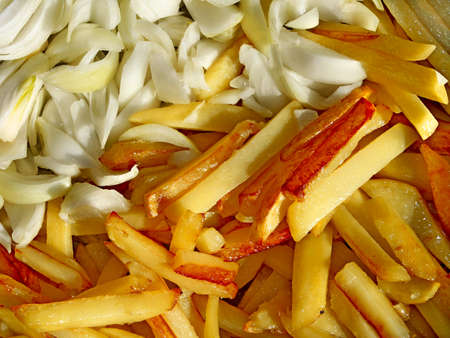 Fried potato chips with golden crust and cutting onions while cooking close-up, in bright sunlightの写真素材