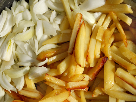 Fried tasty potato chips with golden crust and cutting white onions while cooking close-up, in bright sunlightの写真素材