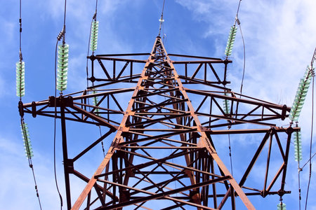 High-voltage electric lattice tower with wires and insulators against the sky